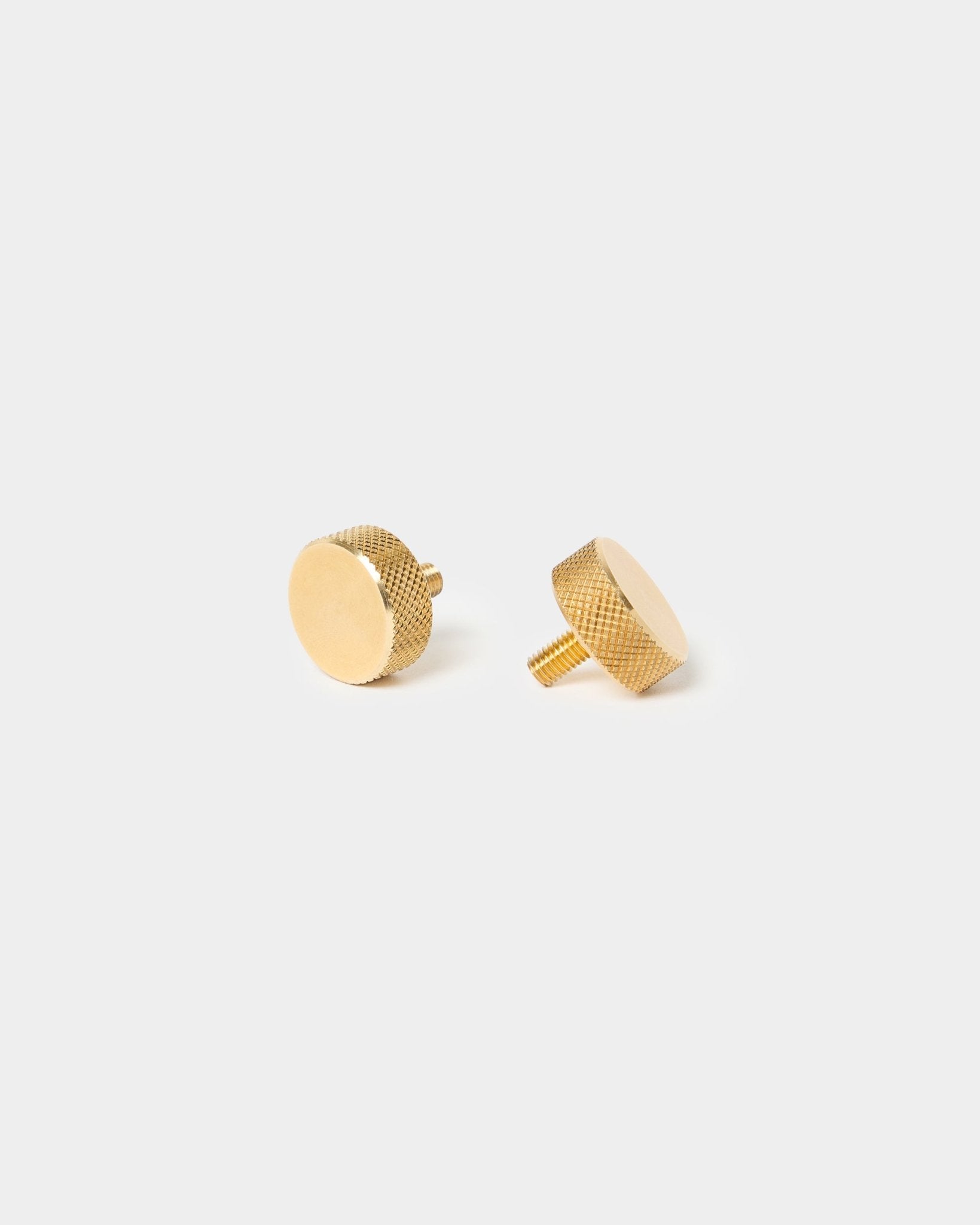Par de tornillos moleteados WoodUpp brass (M5x10 mm, 20x8.8), con bordes texturizados y vástagos cortos, diseñados para accesorios Akupanel, sobre un fondo liso y claro.